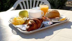 A breakfast tray with croissant, fruit, juice, and yogurt on a white chair outdoors. - Kyriad Direct Agen-Castelculier (Castelculier)