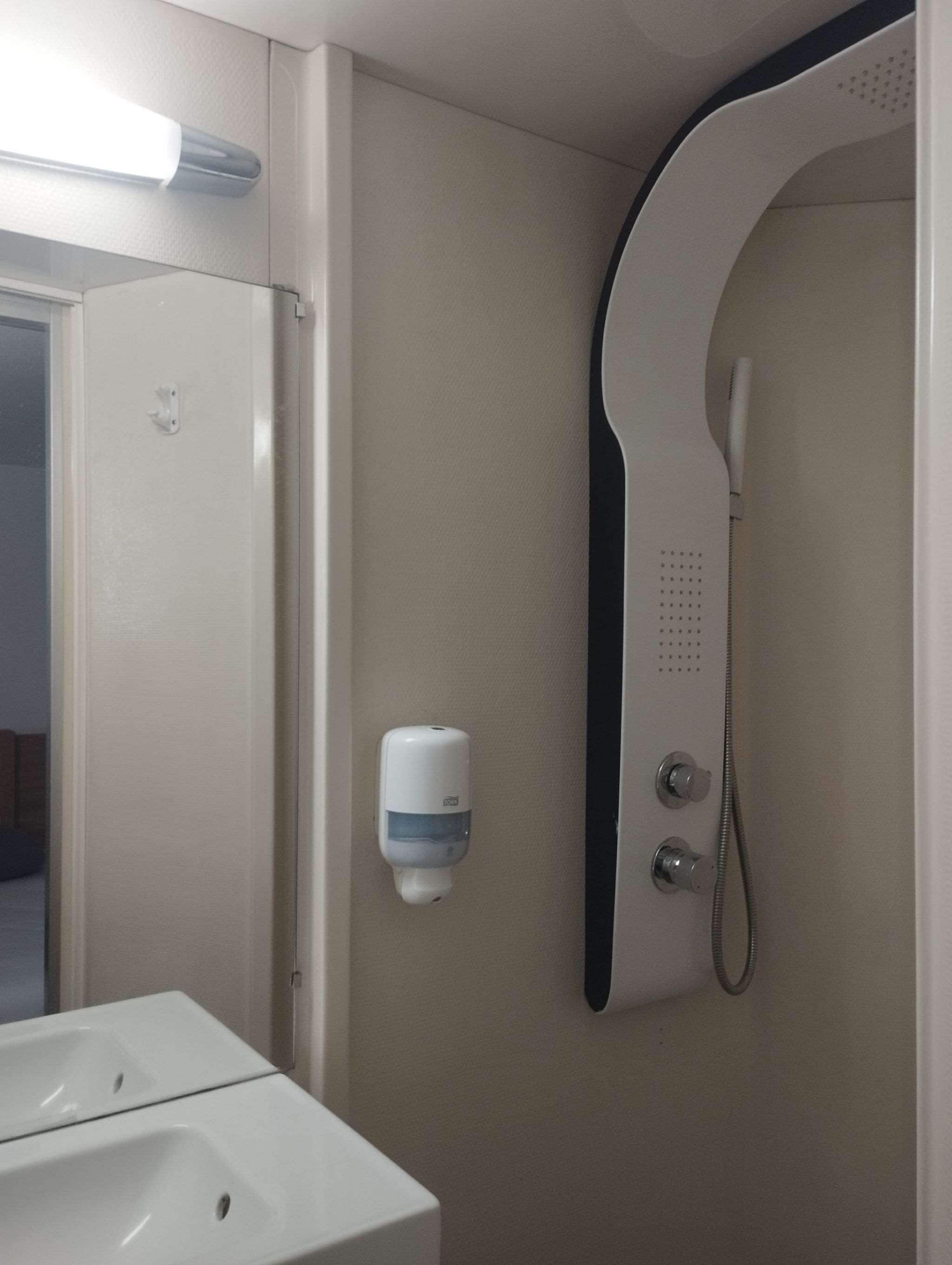 A bathroom with a sink, a soap dispenser, and a shower with a handheld showerhead.