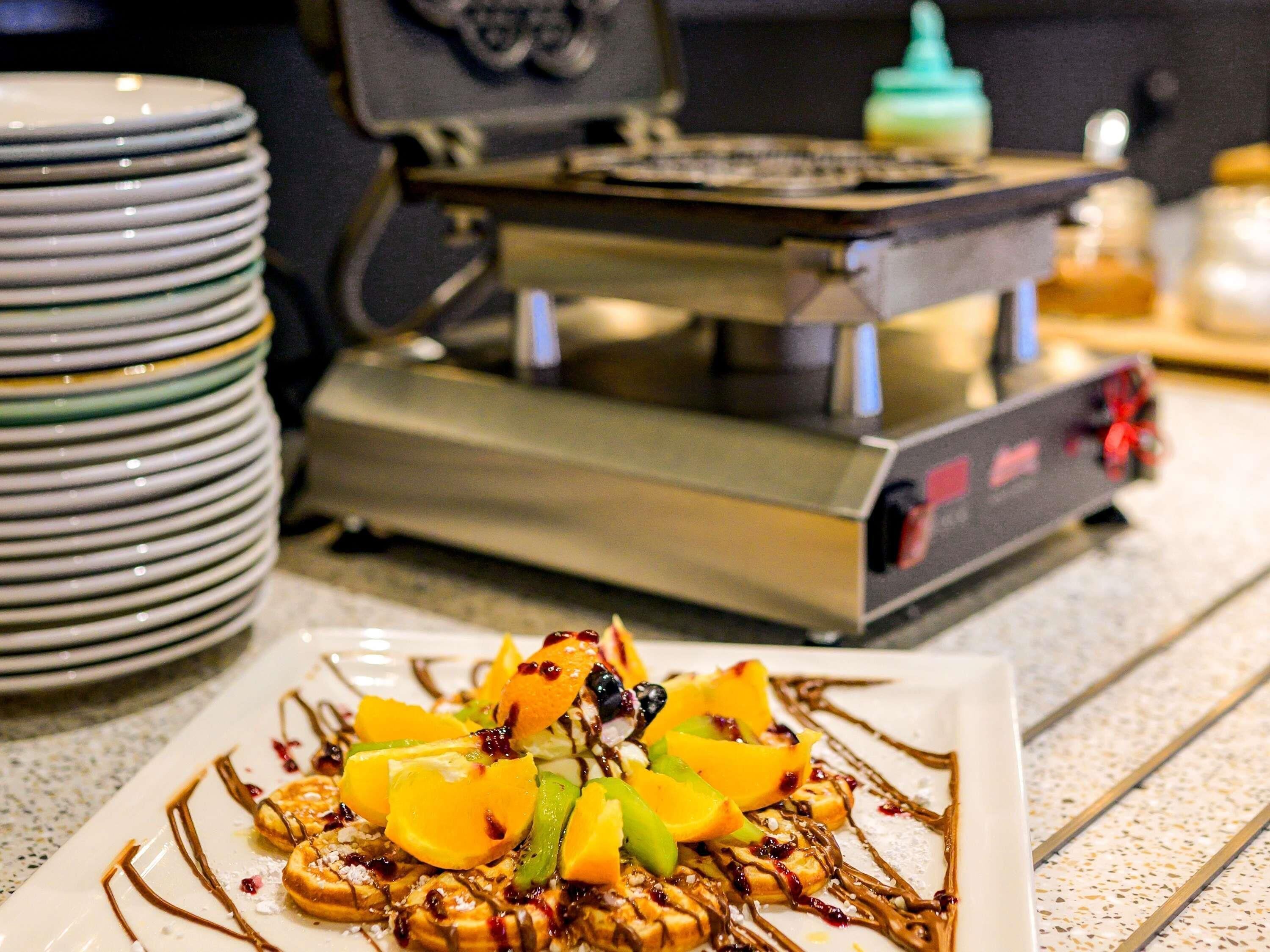 Una pila de platos con un gofre, fruta y un chorrito de chocolate.