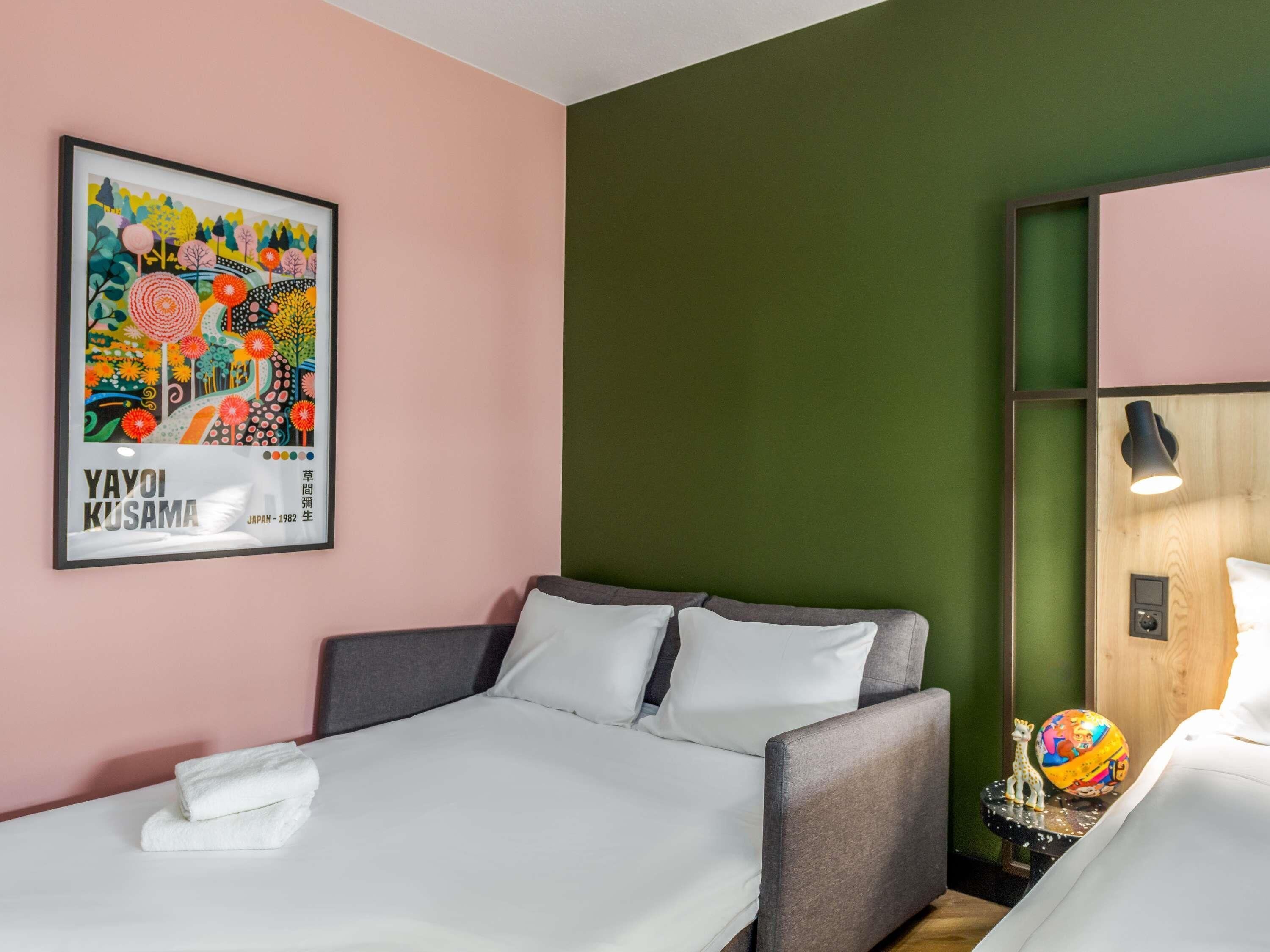 A hotel room with a bed, a pillow, a towel, a wall art piece, and a nightstand with a lamp and a decorative item.