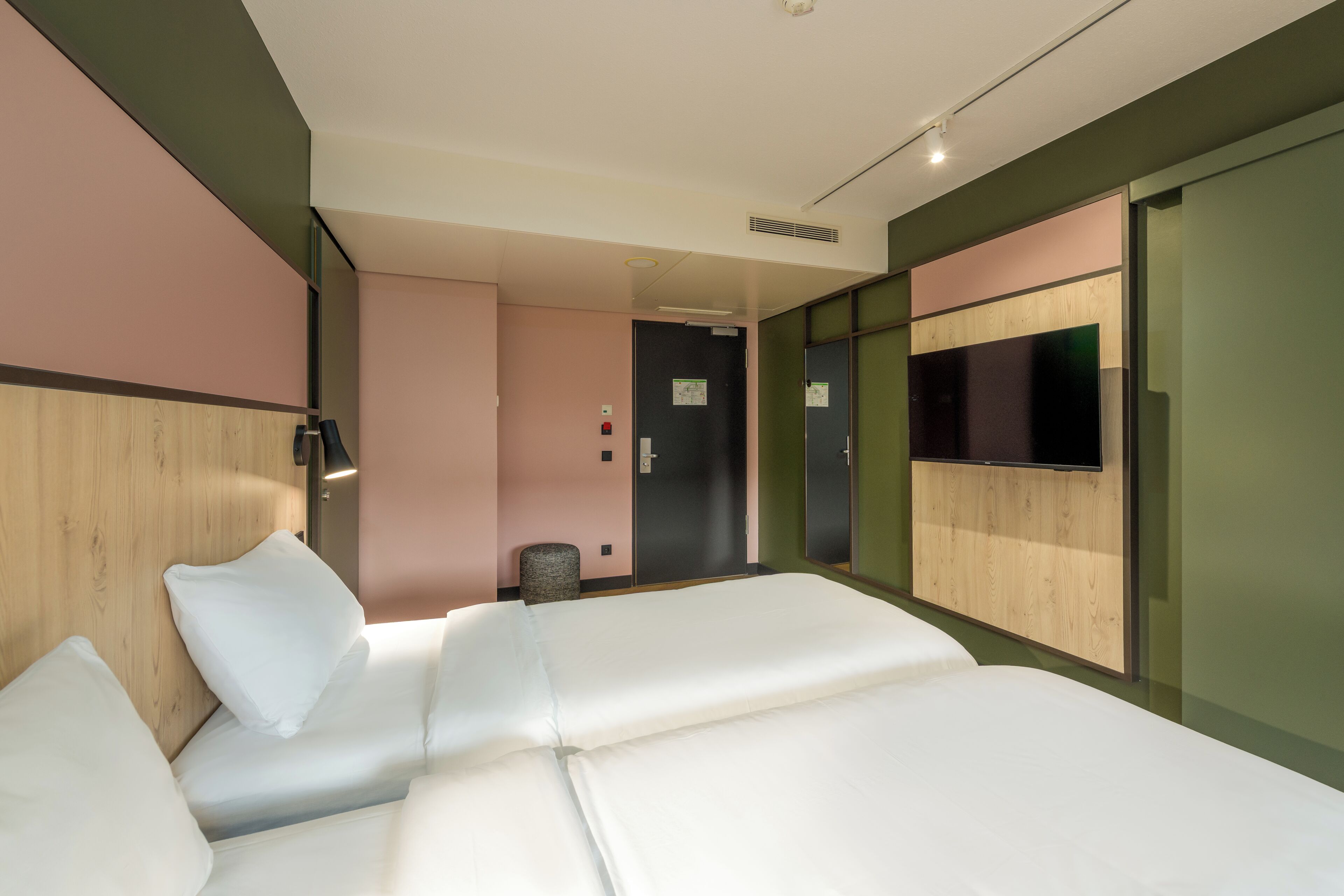 A hotel room with a bed, a flat-screen TV mounted on the wall, and a door leading to a bathroom.