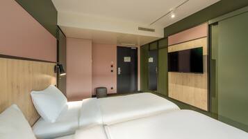 A hotel room with a bed, a flat-screen TV mounted on the wall, and a door leading to a bathroom.