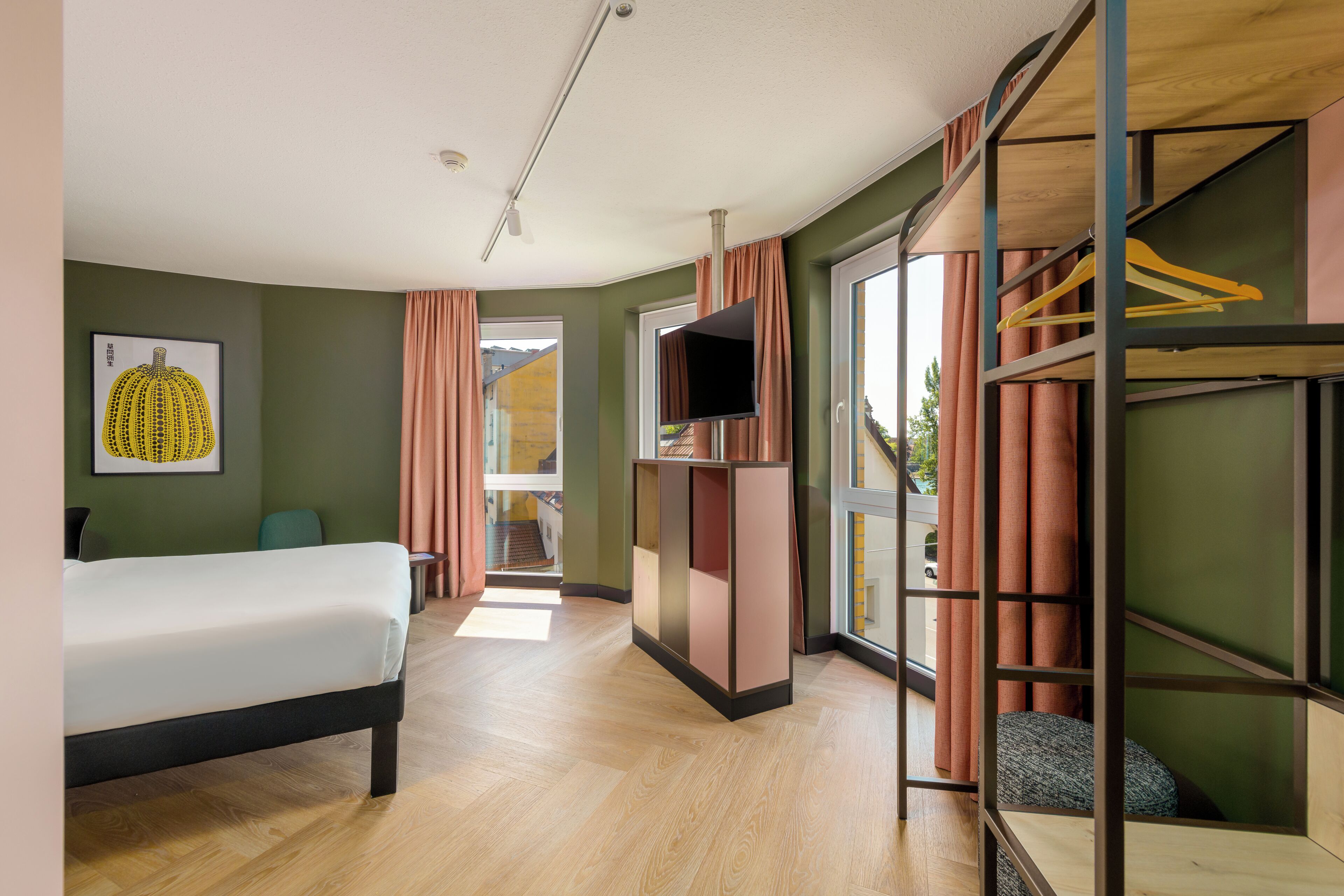 Una habitación de hotel con cama, televisor, armario y ventana con cortinas.