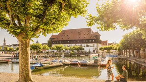 A riverside scene with boats docked, a large building in the background, and a tree in the foreground. - ibis Konstanz (Konstanz)