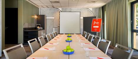 A conference room with a long table, chairs, a projector screen, and a 'SPEAK TO ME' sign.