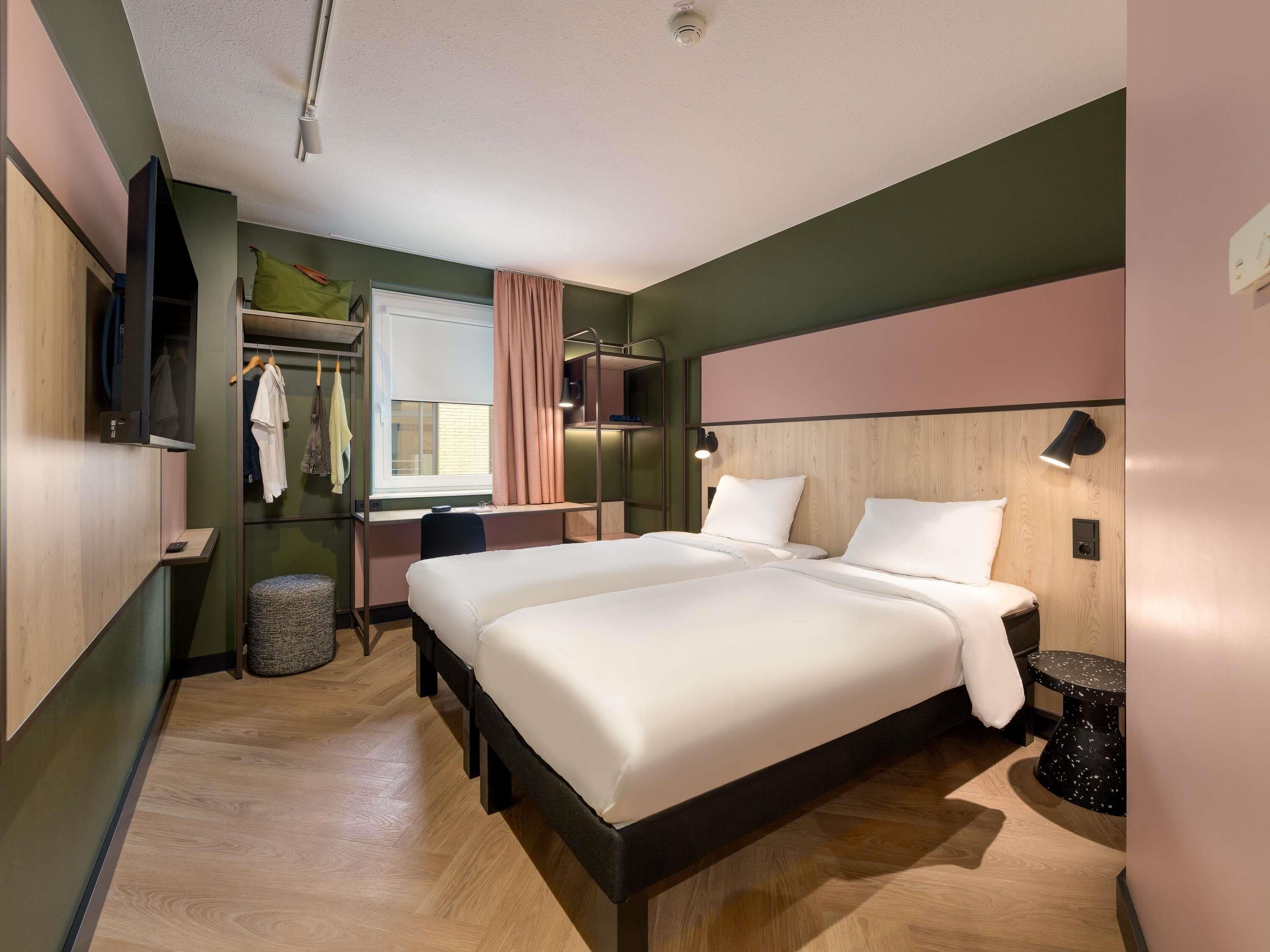 Ein modernes Hotelzimmer mit einem großen Bett, einem Schreibtisch, einem Kleiderschrank und einem Fernseher.