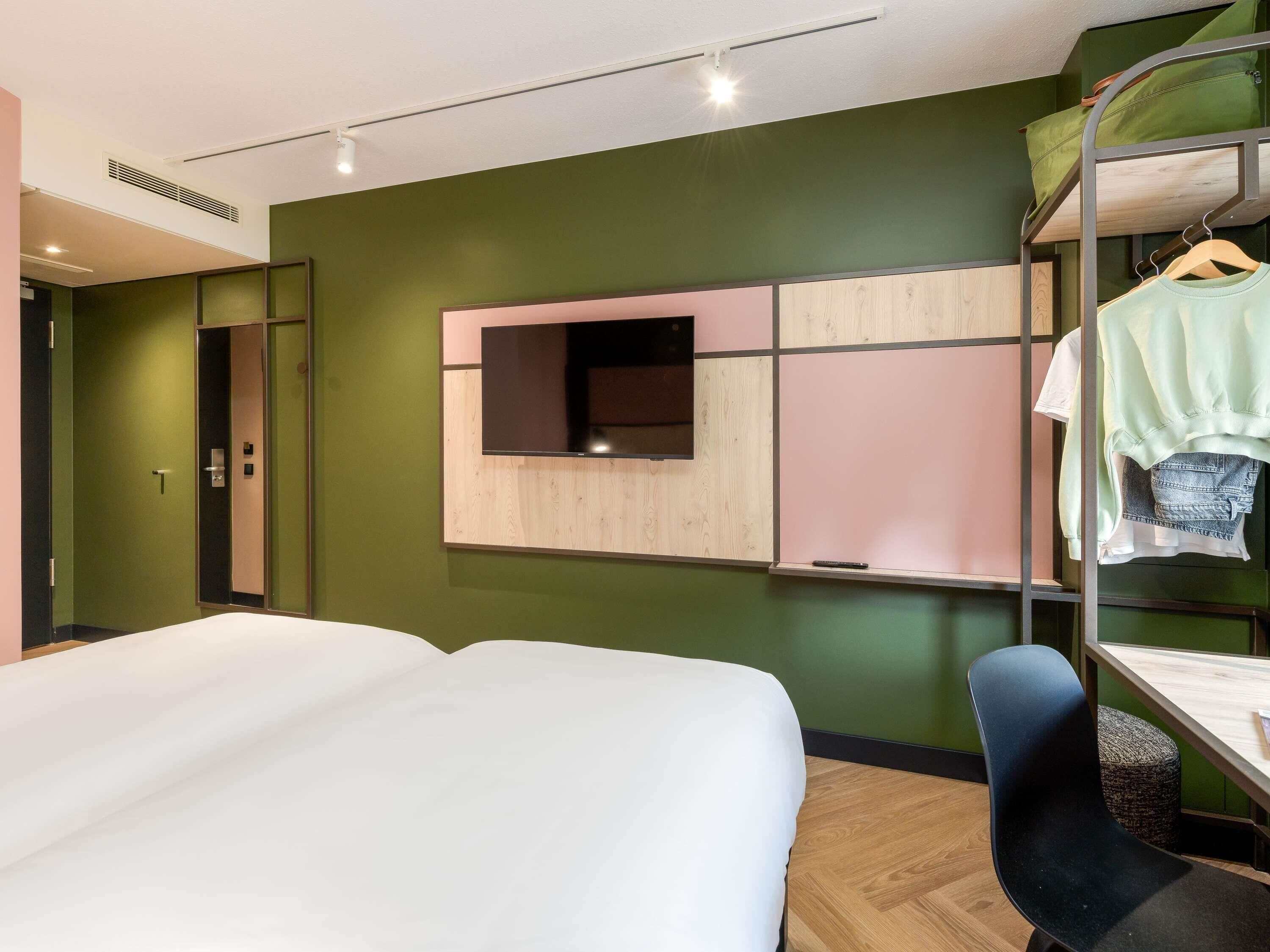 Hotelkamer met een bed, een bureau, een stoel, een kledingkast en een aan de muur bevestigde televisie.