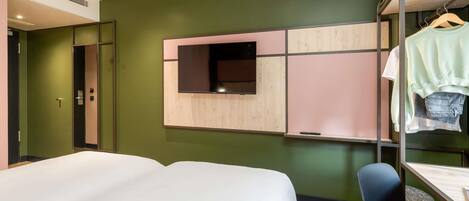 Habitación de hotel con cama, escritorio, silla, armario y televisión instalada en la pared.