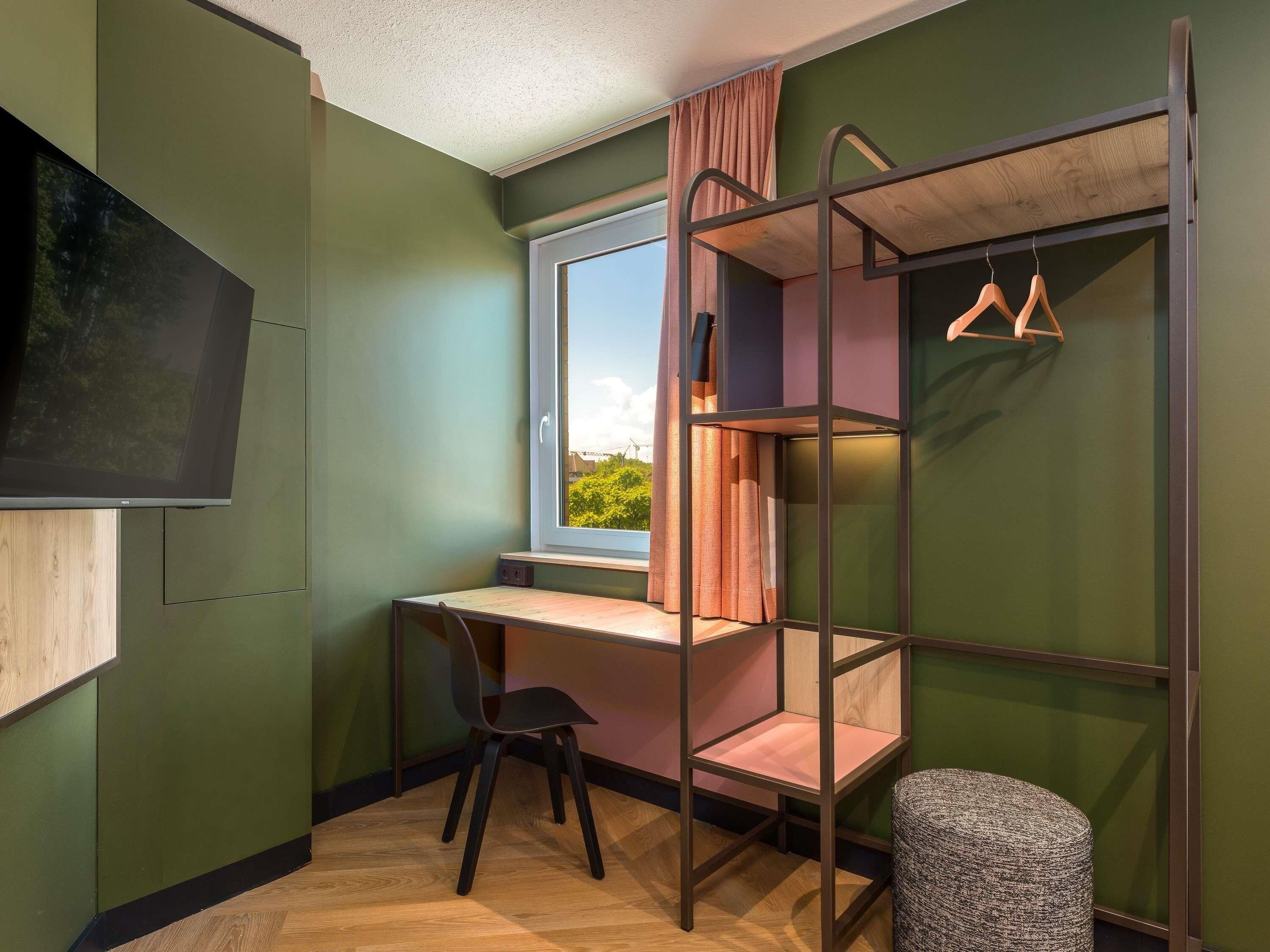 A room with a bunk bed, a desk, a chair, a television, and a window with curtains.