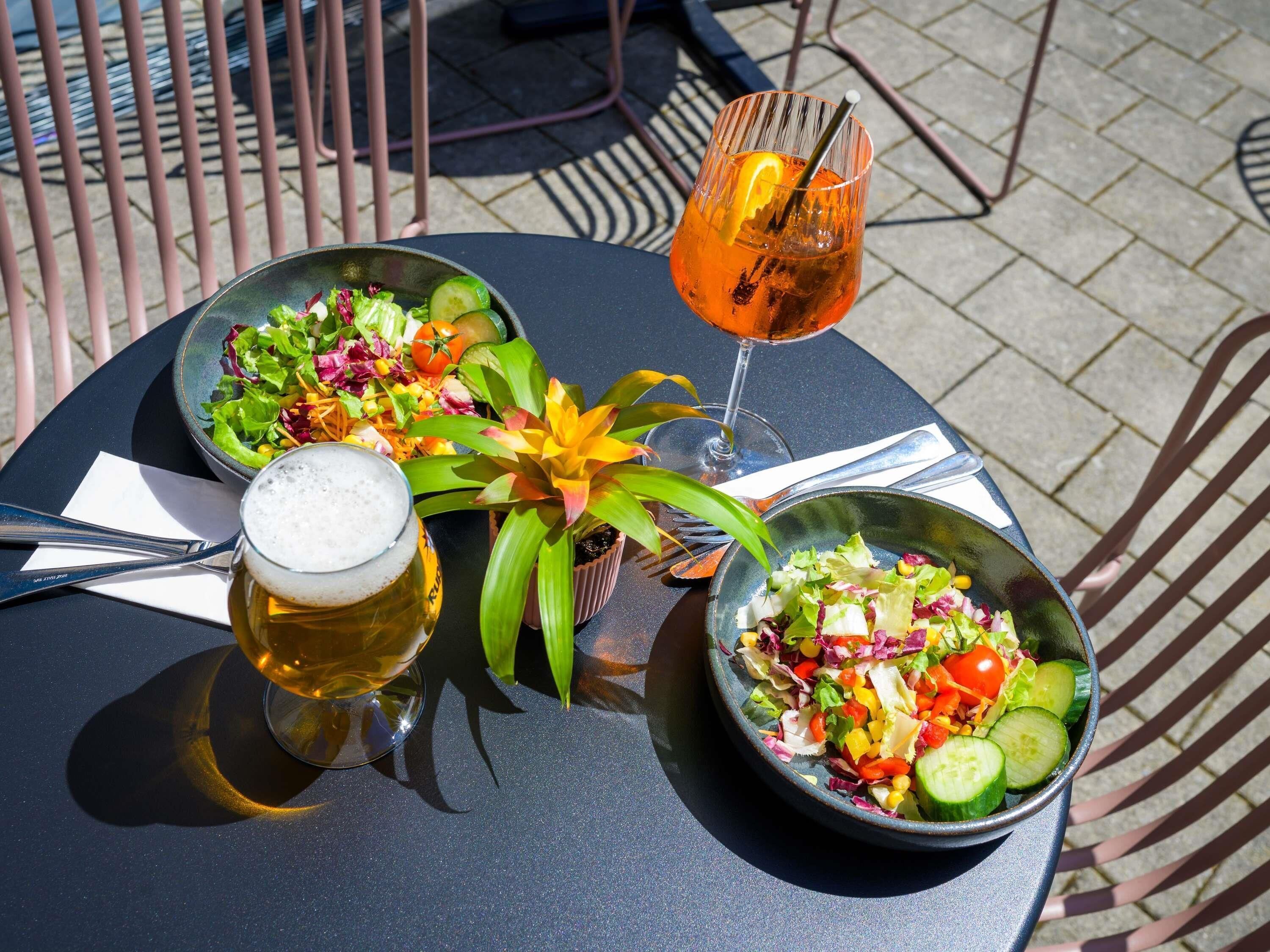 A round table with two bowls of salad, a glass of beer, and a glass of a dark beverage with a lemon slice.