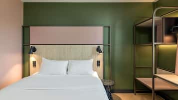 Una habitación de hotel con una cama litera, un cabecero de madera, dos lámparas de noche y una mesita redonda.