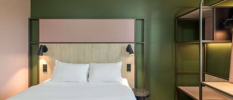Una habitación de hotel con una cama litera, un cabecero de madera, dos lámparas de noche y una mesita redonda.