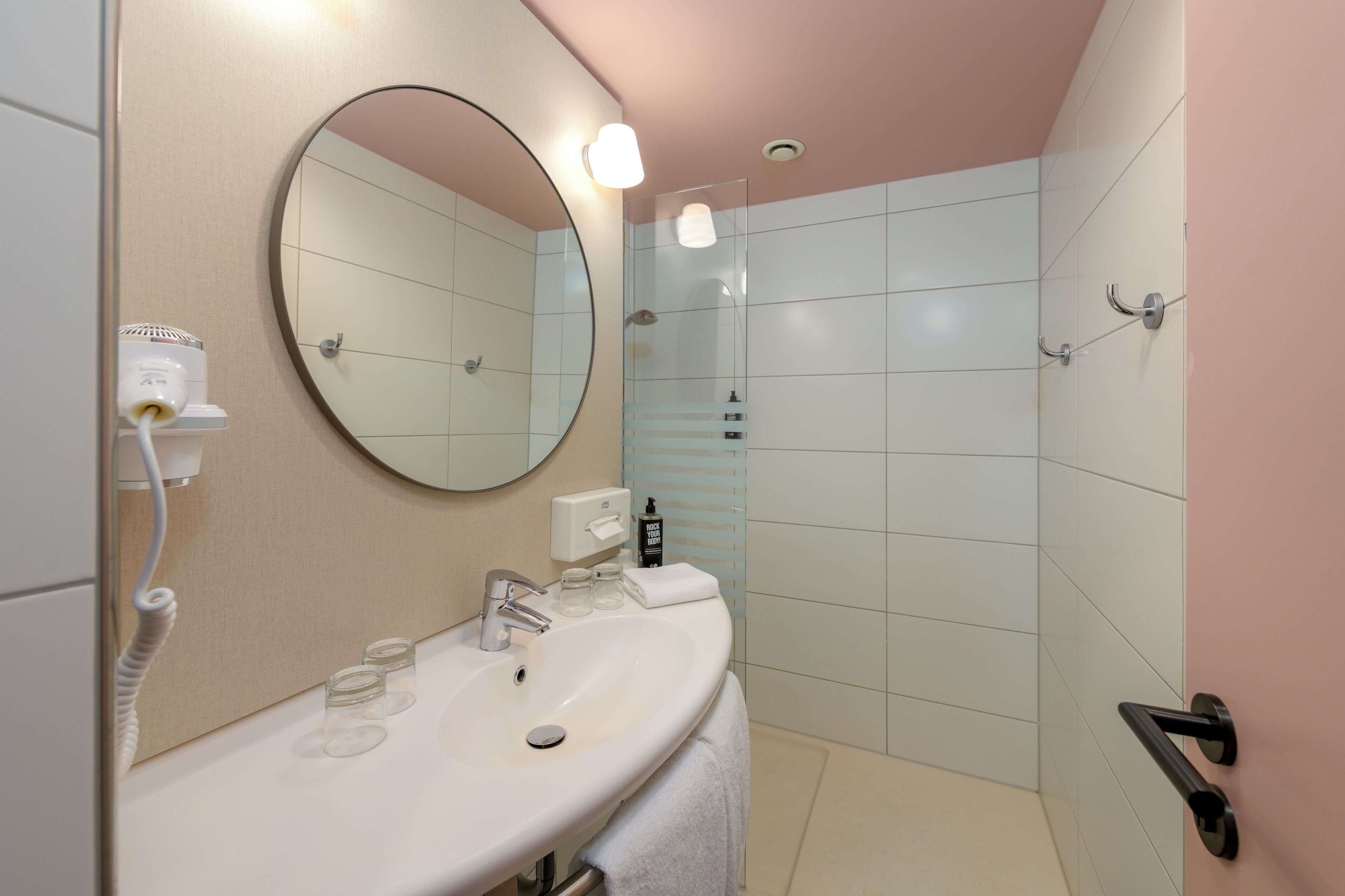A modern bathroom with a round mirror, a sink, and a glass shower enclosure.