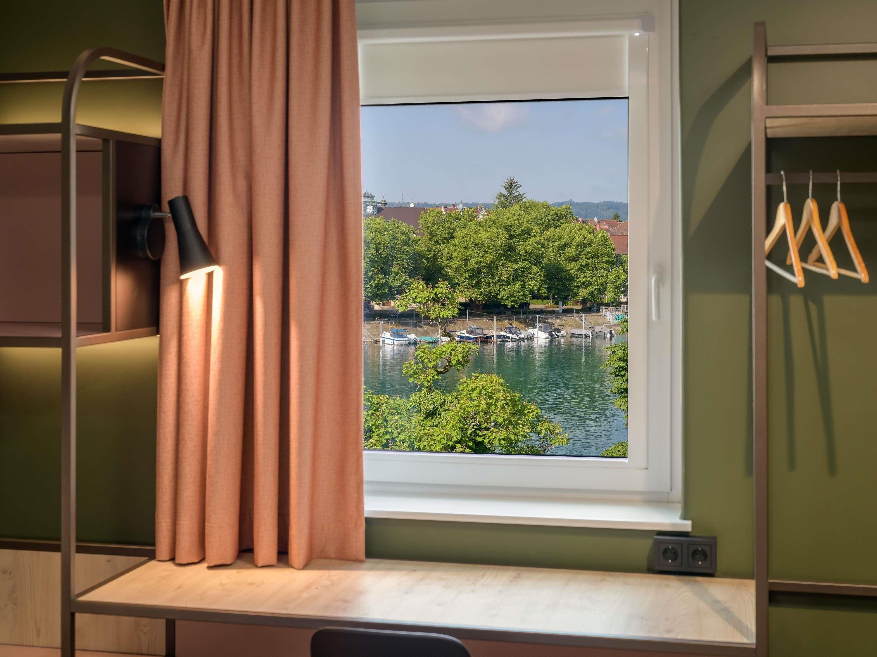 A room with a window overlooking a body of water, a desk, and a hanging chair.