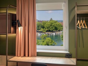 A room with a window overlooking a body of water, a desk, and a hanging chair. - ibis Konstanz (Konstanz)
