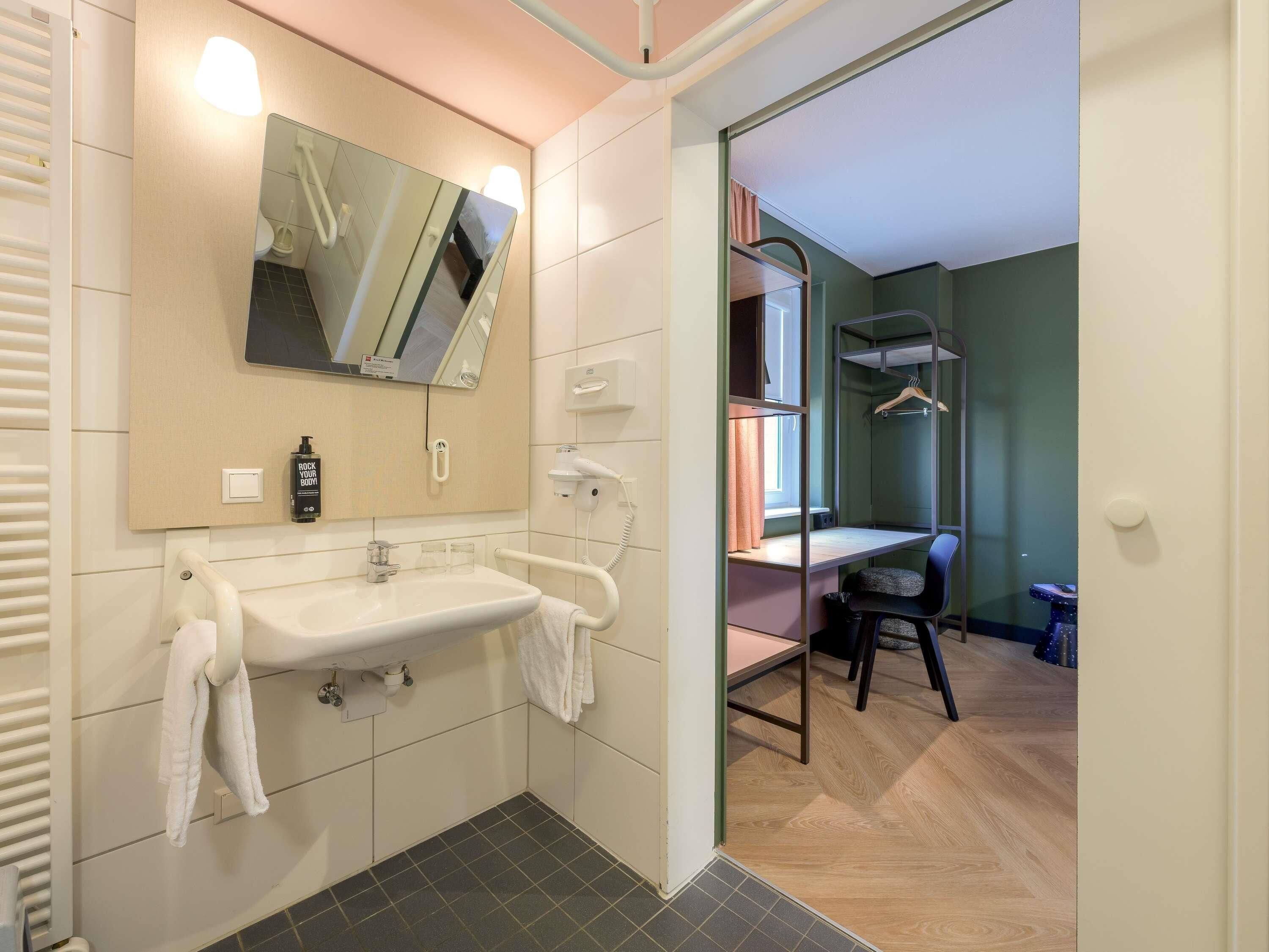 Un baño moderno con lavamanos, espejo y toallero.