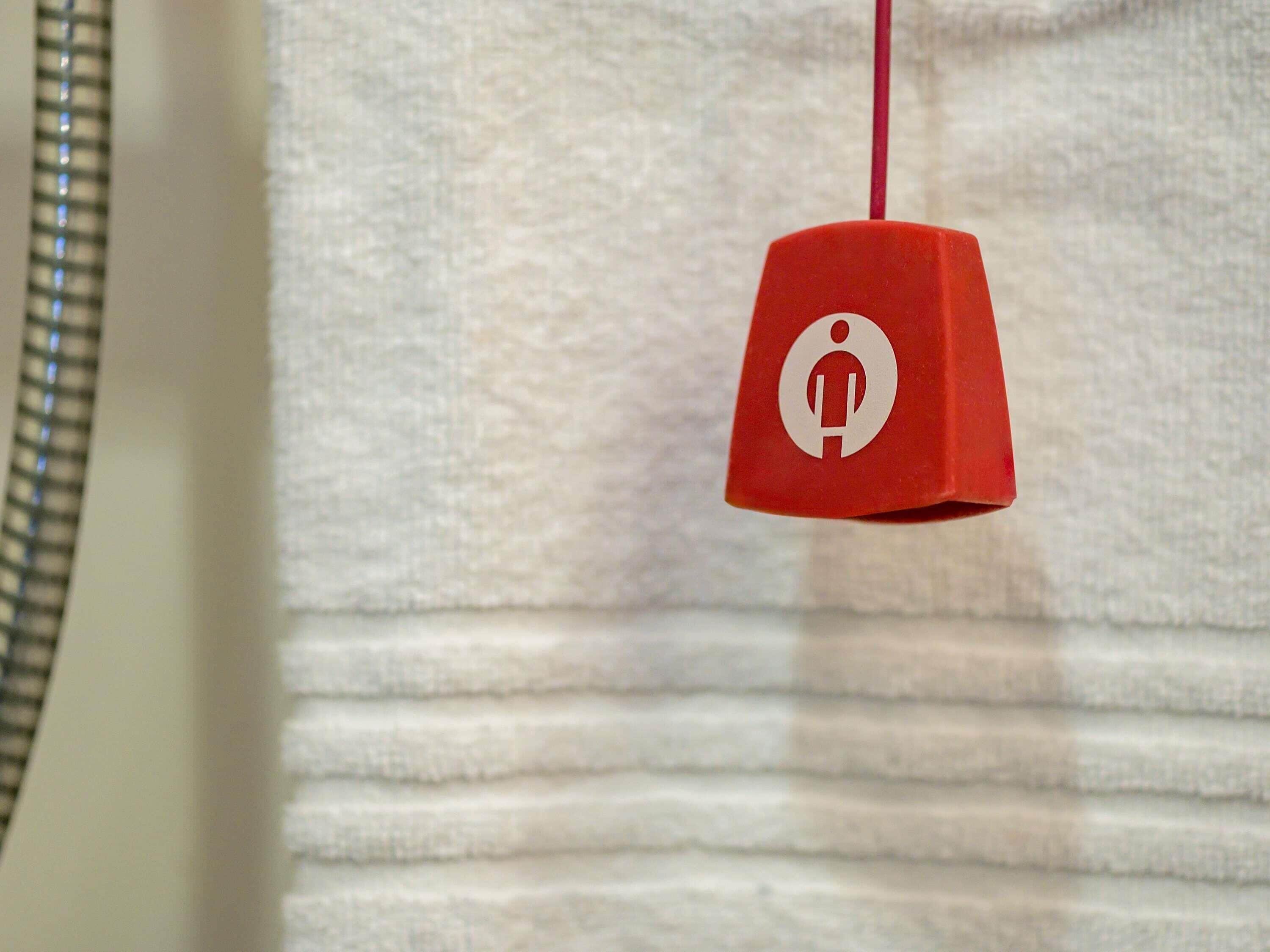 Une sonnette d’alarme rouge, ornée d’un pictogramme blanc, est suspendue à un mur texturé.