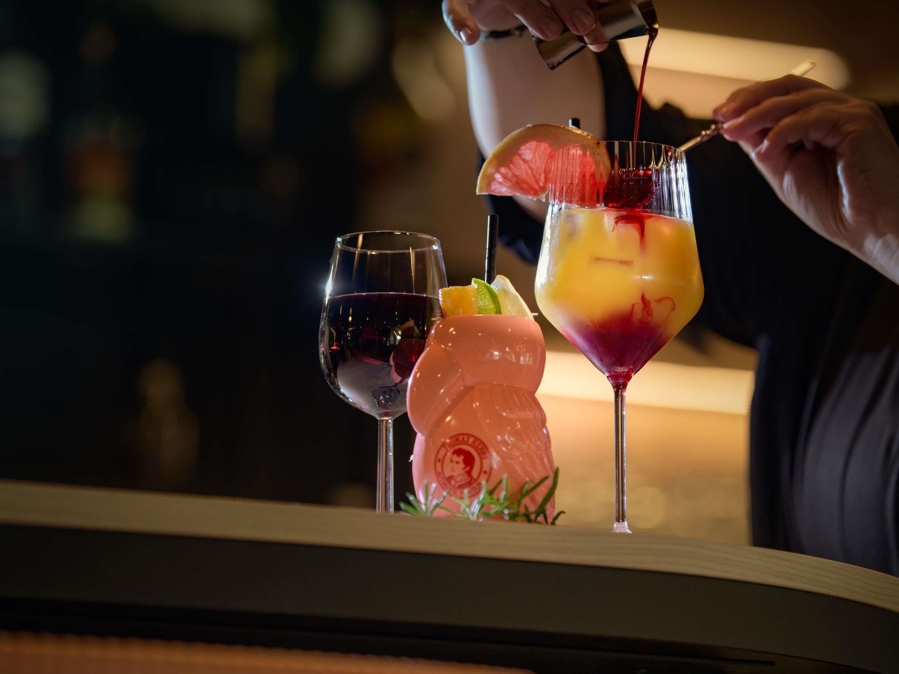 A bartender pouring a drink into a glass with a slice of orange and a rose garnish.