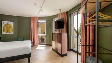 A hotel room with a bed, a TV, a wardrobe, and a view of the outside.
