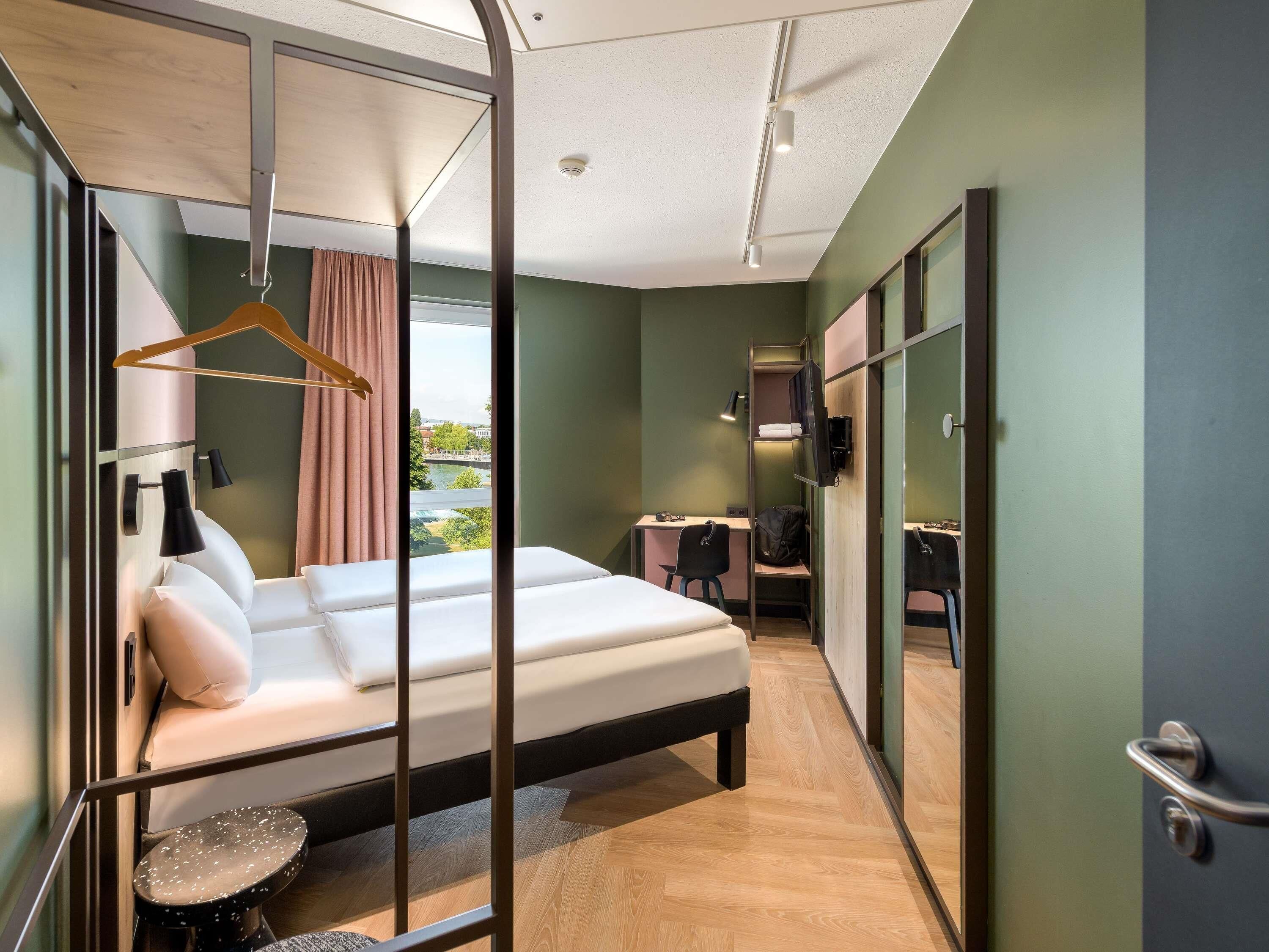 Habitación de hotel con cama, escritorio, silla, televisor y vista al río.