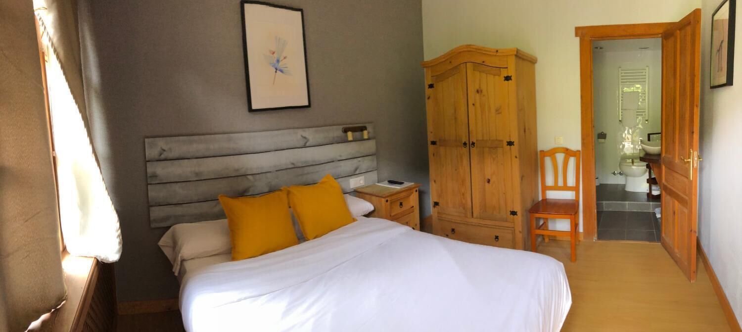 A bedroom with a bed, a wooden wardrobe, a bedside table, and a chair.