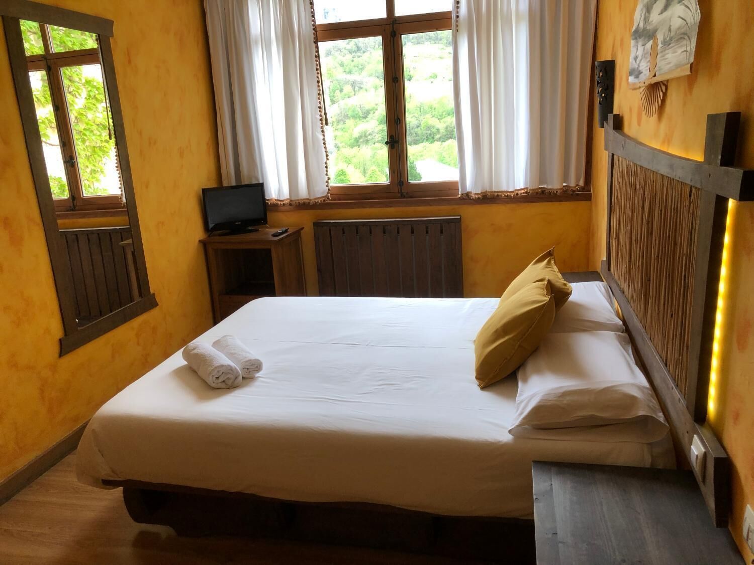 A hotel room with a bed, a TV, a small table, and a window with curtains.