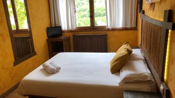 A hotel room with a bed, a TV, a small table, and a window with curtains.