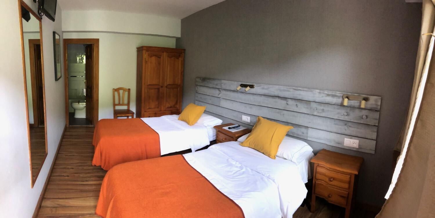A hotel room with two beds, wooden headboard, bedside tables, and a wardrobe.