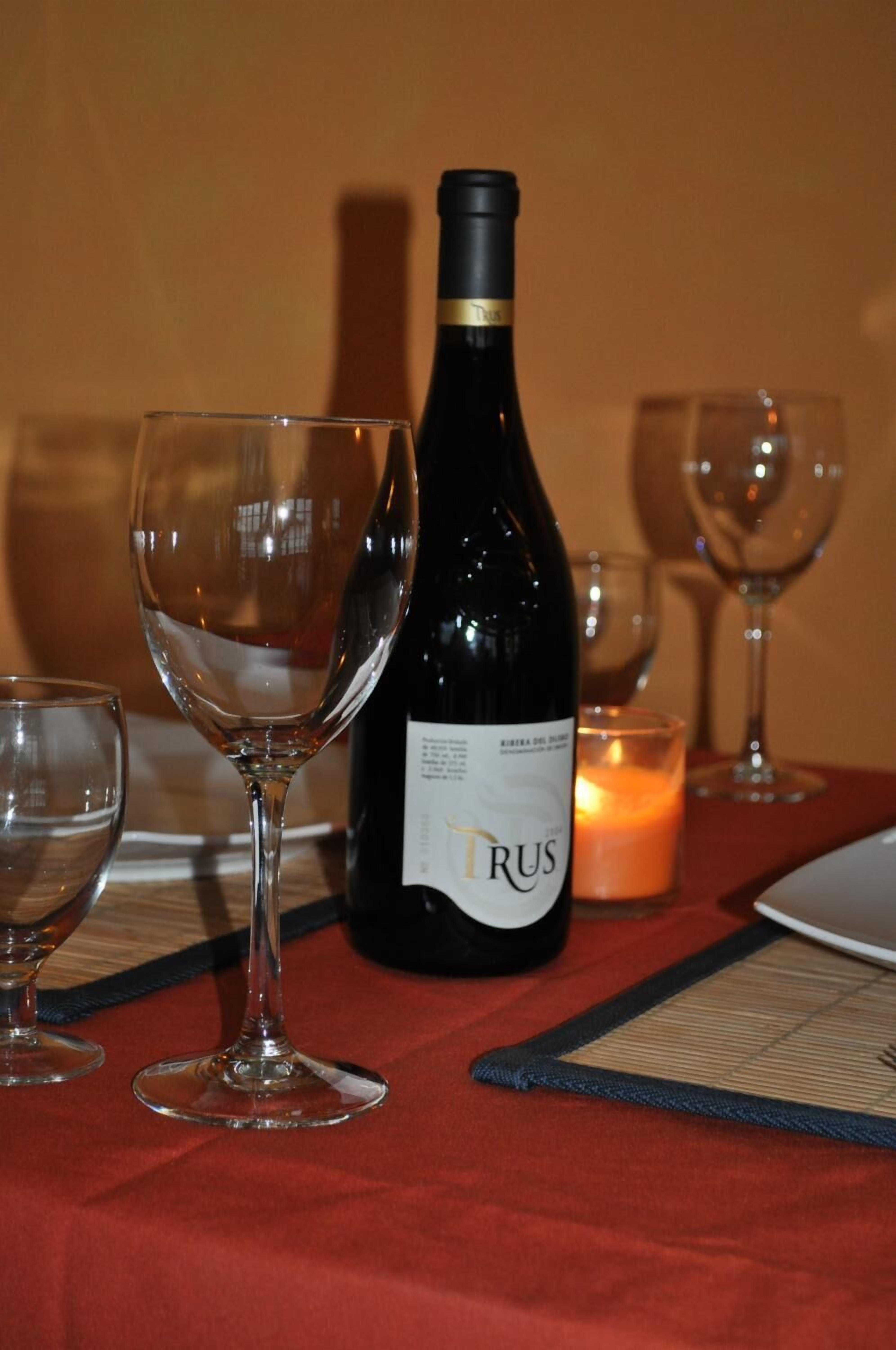 Una mesa servida con una botella de vino, una copa y una vela.