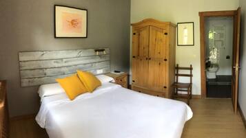 A bedroom with a wooden headboard, a bed with white bedding and yellow pillows, a wooden wardrobe, and a bathroom visible through an open door.