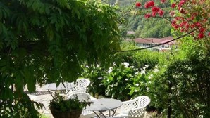Un jardín con un camino de piedra, sillas de plástico blanco y una cesta de flores colgante.