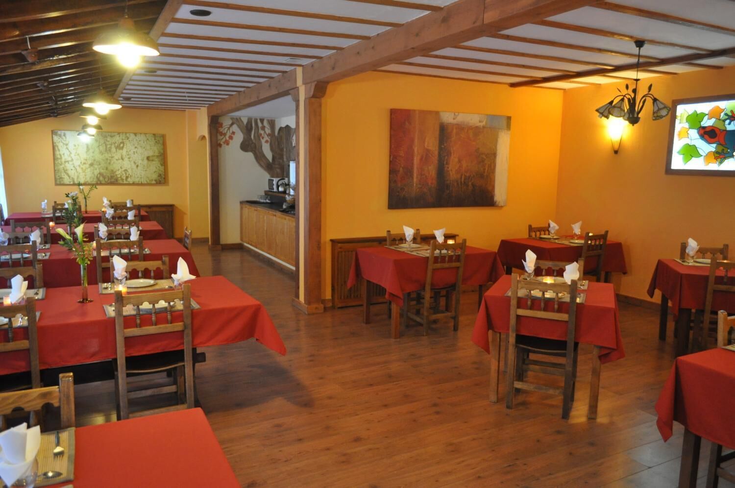 A restaurant with wooden tables and chairs, red tablecloths, and a warm interior.