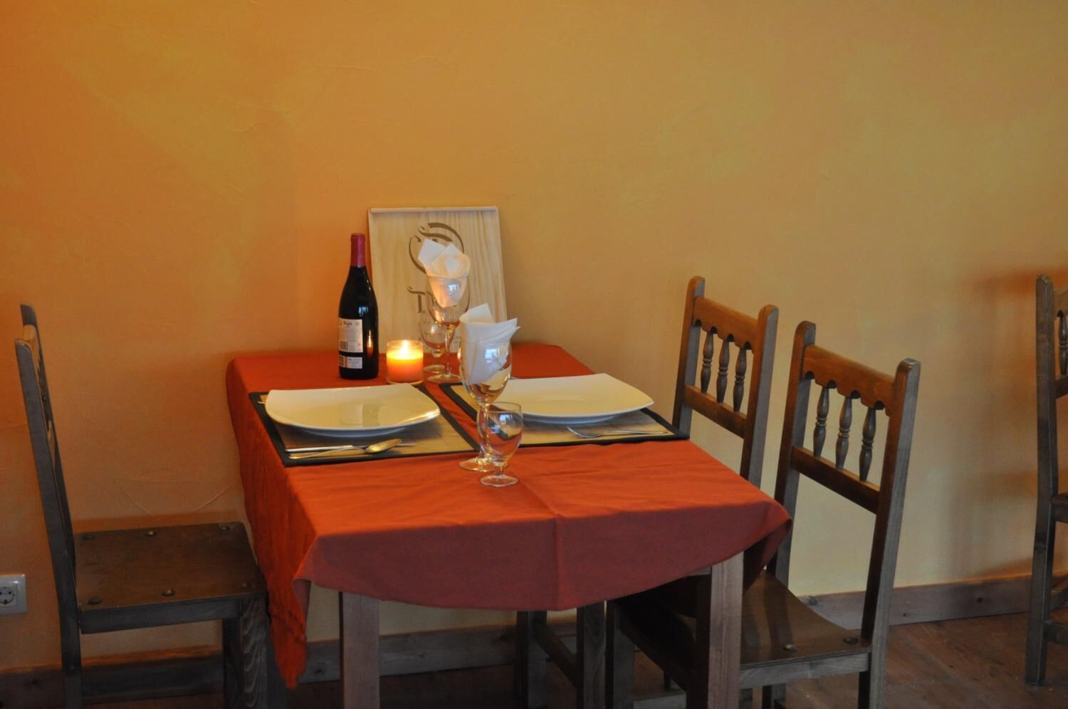Una mesa de comedor dispuesta con platos, una botella de vino, una vela y una copa.