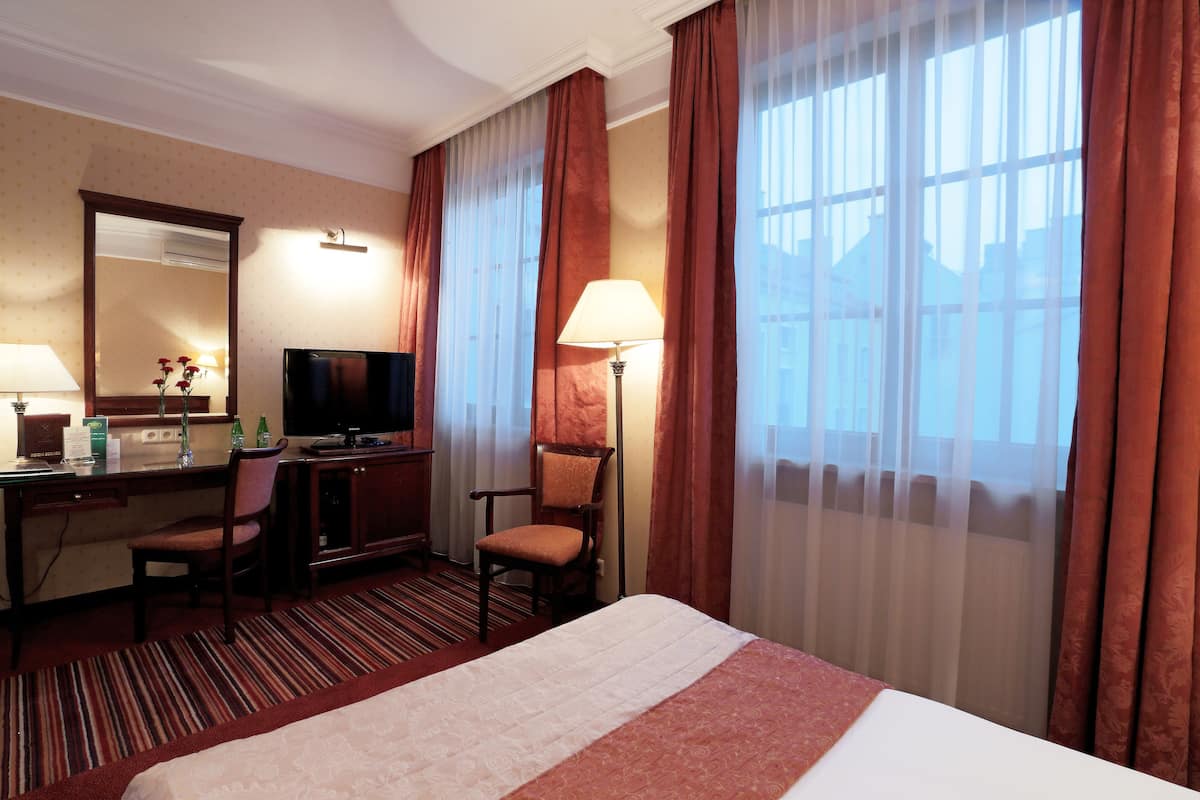 Ein Hotelzimmer mit einem Bett, einem Schreibtisch mit Computer, einem Sessel, einem Fernseher und einem Fenster mit Vorhängen.