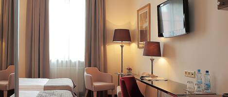Ein Hotelzimmer mit einem Bett, zwei Stühlen, einem Schreibtisch, einem Fernseher und einem Fenster mit Vorhängen.