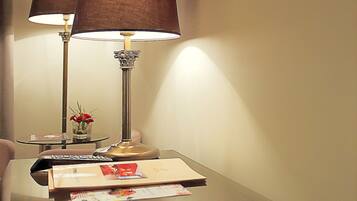 Una habitación de hotel con un espejo, una lámpara, un florero con flores y un televisor de pantalla plana montado en la pared.
