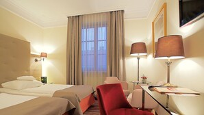 A hotel room with two beds, a desk, a chair, a lamp, and a window with curtains. - Hotel Branicki (Bialystok)