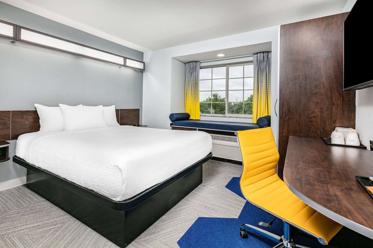 A modern hotel room with a large bed, a desk, and a window with curtains.