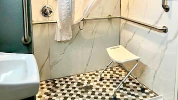 A bathroom with a shower, grab bars, a small stool, and a tiled floor.