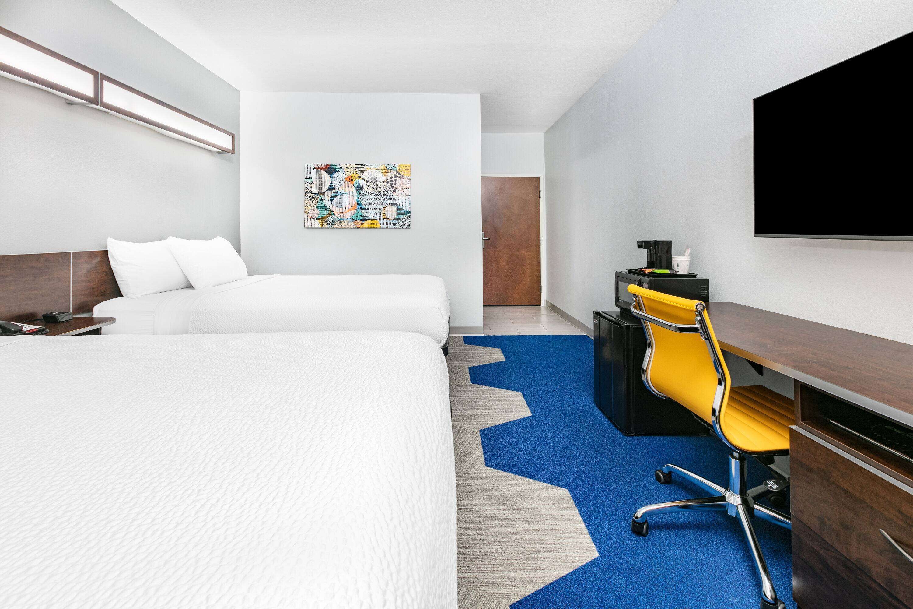 A hotel room with a large bed, a desk with a chair, a flat-screen TV, and a wall-mounted artwork.