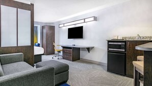 A hotel room with a bed, a gray sofa, a desk with a chair, a television, a microwave, and a small refrigerator. - Microtel Inn & Suites by Wyndham Austin Airport (Austin)