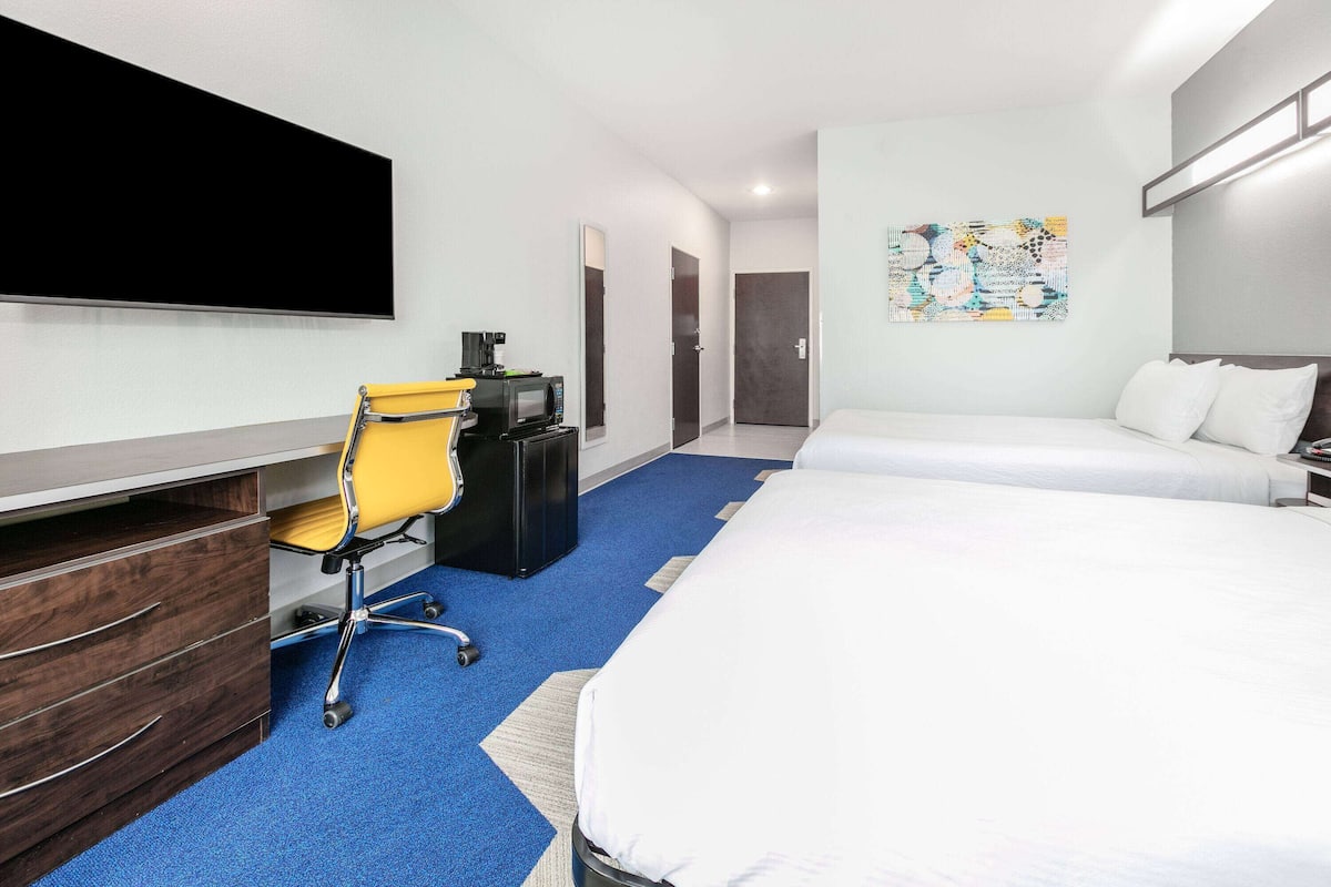 A hotel room with a bed, a desk with a chair, a TV, and a coffee machine.
