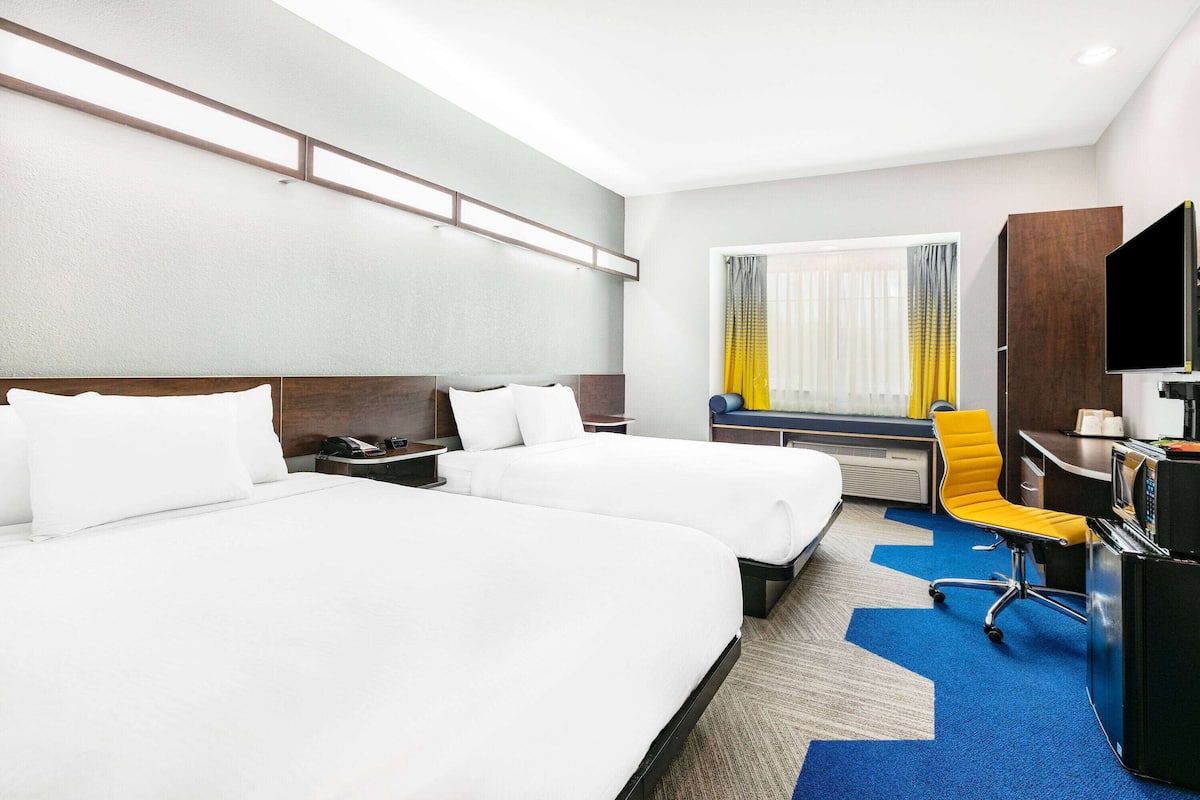 A hotel room with two beds, a desk with a chair, a television, and a window with curtains.