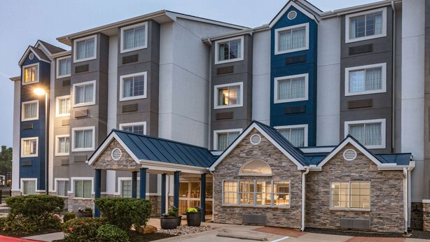 A multi-story hotel with a stone facade and a blue roof. It features a parking lot with handicapped accessibility. - Microtel Inn & Suites by Wyndham Austin Airport (Austin)