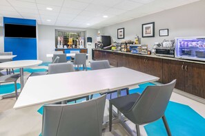A modern dining area with a long white table, grey chairs, and a blue accent wall. - Microtel Inn & Suites by Wyndham Austin Airport (Austin)