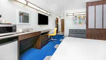 Habitación de hotel con cama, escritorio con microondas, silla, televisión y baño.