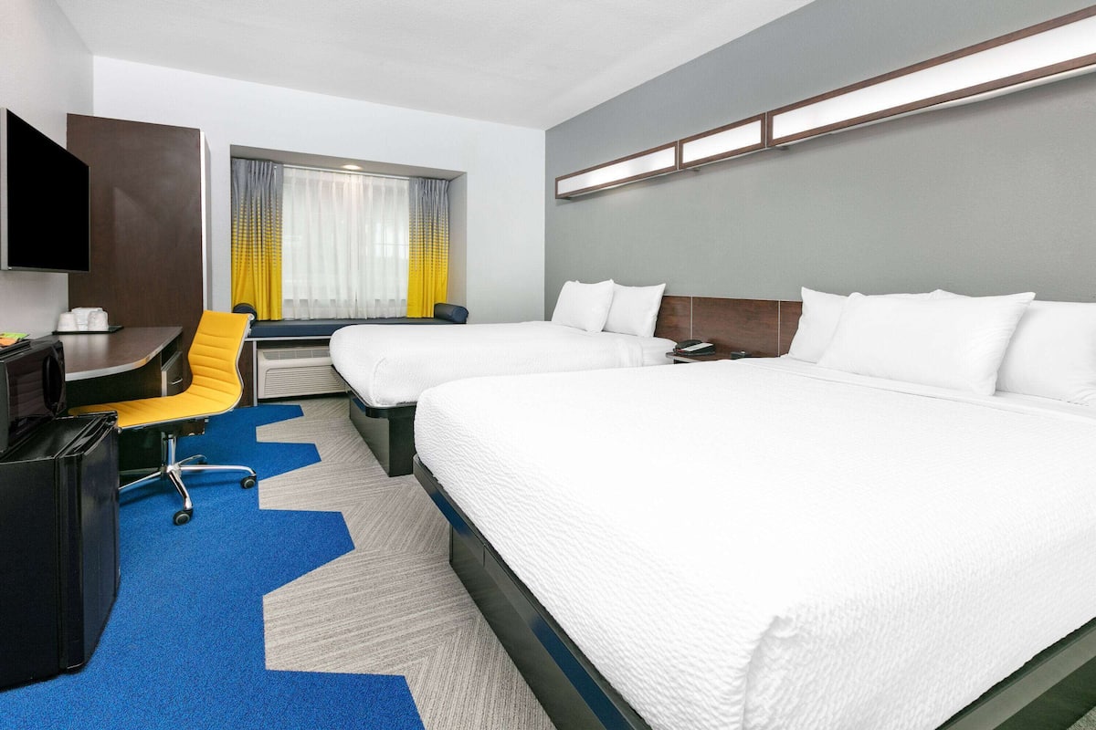 A hotel room with two beds, a desk, a chair, a TV, and a window with curtains.