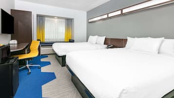 Habitación de hotel con dos camas, un escritorio, una silla, un televisor y una ventana con cortinas.