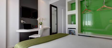 Une chambre d’hôtel moderne équipée d’un lit, d’un bureau avec un ordinateur portable, d’une télévision et d’un mur d’accent vert.