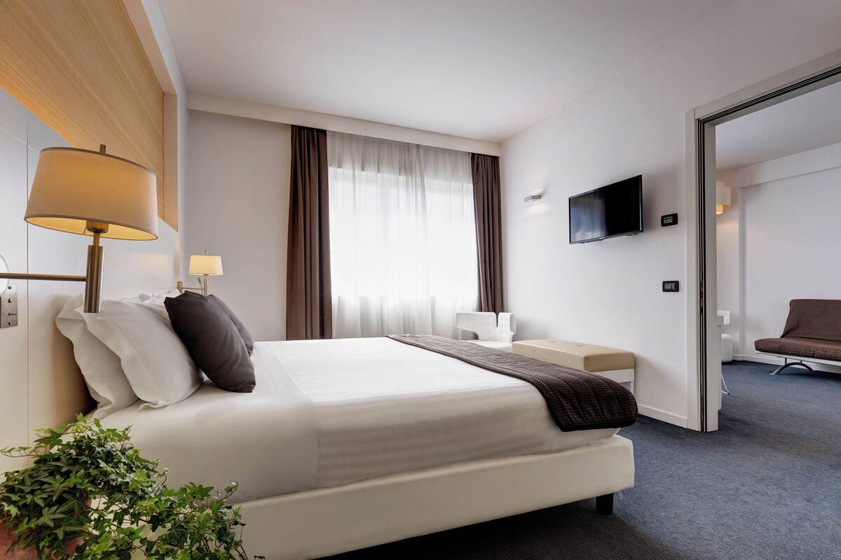 A hotel room with a bed, bedside lamps, a TV, a desk, and a chair.